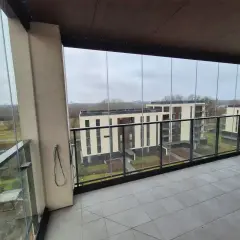 Zabudowa balkonu w bloku z widokiem na nowoczesne budynki. Szklane panele tworzą przestronną loggię.