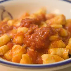 Pyszne gnocchi alla sorrentina w sosie pomidorowym, podane w białej misce z niebieskim rantem.