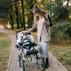 Mama poprawia czapkę malucha, który siedzi w spacerówce. Jesienny spacer po parku.