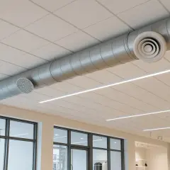 Conductos metálicos para sistemas de ventilación y extracción de aire, visibles en un techo suspendido con iluminación lineal.