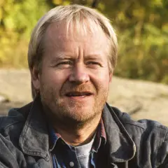 En leende svensk manlig skådespelare från 2000-talet, med blont hår och skäggstubb, bär en jeansjacka.