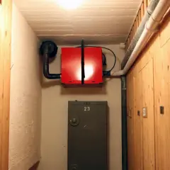 Röd radonfläkt monterad på väggen i en källarkorridor med träpaneler. En ventilationstrumma leder bort luften.