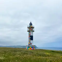 Faro colorido en el cabo de Ajo, con un paisaje verde y el mar al fondo.