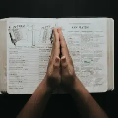 Dłonie złożone w modlitwie nad otwartą Biblią, w której widnieje porównanie Starego i Nowego Testamentu. To chwila refleksji i psalmy uwielbienia.
