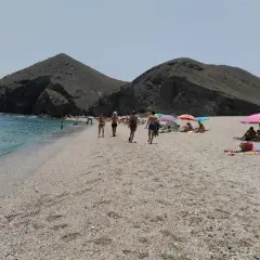 Gente disfrutando del sol y el mar en la playa de los Muertos en Carboneras, con sus icónicas montañas de fondo.