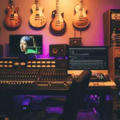 Guitars suspendus au-dessus d'une console de mixage, d'écrans et de racks d'équipement studio d'enregistrement, baignant dans une lumière violette.