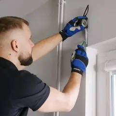 Mężczyzna w rękawiczkach mierzy ścianę taśmą i zaznacza ołówkiem miejsce montażu karnisza.