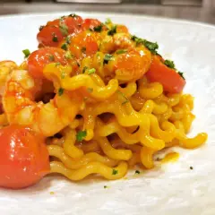 Un piatto invitante di pasta con gamberetti, pomodorini succosi e un tocco di prezzemolo fresco.