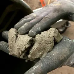 Rękawice robocze trzymają grudki zaschniętego betonu, co jest pierwszym krokiem w procesie, jak wyczyścić betoniarkę.