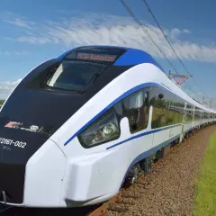 Nowoczesny pociąg Pesa Bydgoszcz ED161-002 mknie po torach wśród pól i zieleni, pod błękitnym niebem z chmurami.