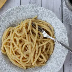 Pyszne cacio e pepe na talerzu z ozdobnym wzorem. Widok z góry na makaron z serem i pieprzem, obok widelec.