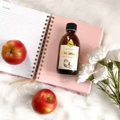 Jabłka i butelka octu jabłkowego na notatniku. Naturalny ocet na skórę, który warto mieć w swojej kosmetyczce.