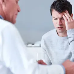 Ein Mann mit Kopfschmerzen spricht mit einem Arzt. Die Diagnose: ein gutartiger hirntumor.