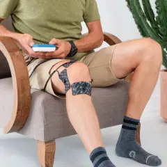 Homme assis, utilisant un appareil d'électrostimulation pour le traitement de sa tendinite au genou.