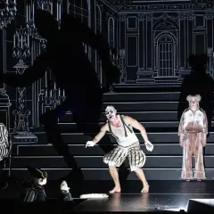 Scen från "Misantropen" på Dramaten. En clownliknande figur, en kvinna i randigt och en äldre kvinna i rosa pyjamas.