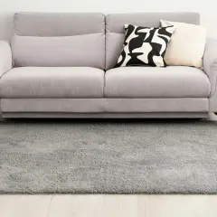 Grauer Hochflorteppich vor einem Sofa. So reinigen Sie Ihren langflorigen Teppich für ein frisches Zuhause.