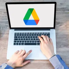 Frustrated hands try to access Google Drive on a laptop, but the screen shows only the logo, suggesting it's not loading.