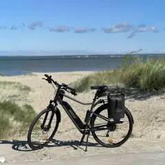 Rower z sakwą czeka na przygodę. Idealna trasa rowerowa nad morzem, z piaszczystymi wydmami i błękitnym niebem.