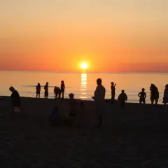 Sylwetki ludzi na plaży o zachodzie słońca nad morzem.