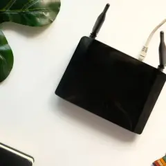 Czarny router z antenkami i kablem. Obok liść, notatnik i kolorowa podkładka. Czy router pobiera dużo prądu?