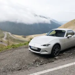 Un Mazda MX5 blanco en una carretera de montaña. Las opiniones sobre este coche son muy positivas, ideal para disfrutar de paisajes así.