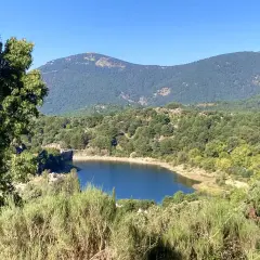 El embalse de Navalmedio, rodeado de bosques y montañas, refleja el cielo azul.