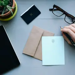 Ręka pisze o uciążliwym sąsiedzie. Na biurku notatnik, okulary, koperta i papeteria.