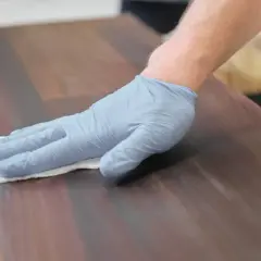 Main tenant une lingette, une main gantée applique un produit sur un beau bois piqué.