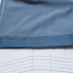 Pins secure the folded hem of blue knit pants, ready for sewing. This image shows a step in how to hem knit pants.