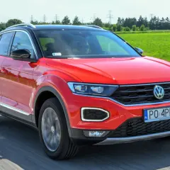 Czerwony volkswagen t-roc używany na drodze, z zielonym polem w tle.