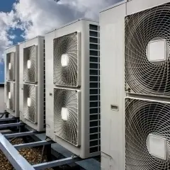 Rząd jednostek klimatyzacyjnych na dachu pod błękitnym niebem z chmurami.