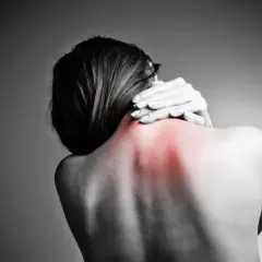 Kobieta masuje obolałą szyję, gdzie widoczny jest czerwony obszar bólu. Może to być objaw spondylozy.