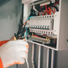 Elektryk w białych rękawicach pracuje przy skrzynce z bezpiecznikami. Zabezpieczenie przedlicznikowe jest kluczowe dla bezpieczeństwa instalacji.
