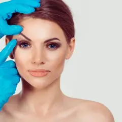 Kobieta z nieudaną plastyką powiek górnych, której oczy są badane przez lekarza w niebieskich rękawiczkach.