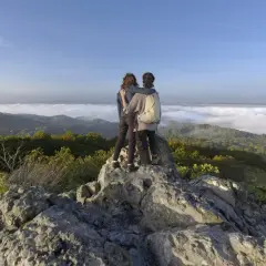 Zwei Freunde genießen den Ausblick beim Wandern an der Sieg. Nebel liegt im Tal, die Sonne scheint auf die Berge.