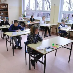 Uczniowie siedzą w ławkach podczas egzaminu szóstoklasisty. Jedna z uczennic zakrywa twarz dłońmi, widać napięcie.