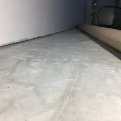 Ojämn betongyta som väntar på att slipa betong för en jämn finish. En rulle skyddspapper ligger längs väggen.