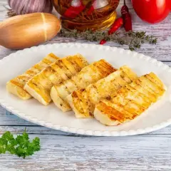 Grillowany ser halloumi na talerzu, idealny do prostych przepisów. W tle czosnek, cebula i pomidory.