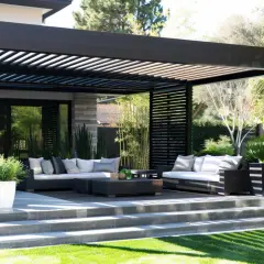 Nowoczesna, czarna pergola przed wejściem do domu, z wygodnymi sofami i stolikami, tworzy idealne miejsce do relaksu na świeżym powietrzu.
