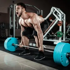 Mężczyzna z determinacją wykonuje deadlift, zaciągając sztangę z niebieskimi talerzami.