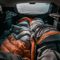 Gemütlich schlafen im Auto, zwei Schlafsäcke liegen bereit. Eine Kamera und Snacks sind auch da für das Abenteuer.