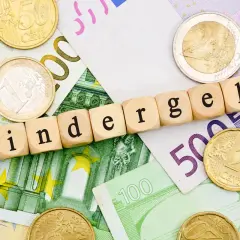 Drewniane klocki z napisem "Kindergeld" leżą na banknotach euro i monetach. Czekamy na Kindergeld 2026!