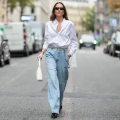 Kobieta w luźnych, jasnych jeansach typu mom fit i białej koszuli, z białą torebką. Stylizacja dla każdej kobiety ceniącej wygodę i modny wygląd.