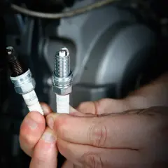 Manos sostienen bujías de moto, una nueva y otra sucia. Saber cada cuanto cambiar bujias moto es clave para el rendimiento.