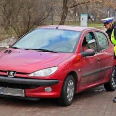 Policjantka kontroluje czerwony samochód. Czy można jeździć bez plastiku po zdaniu egzaminu?