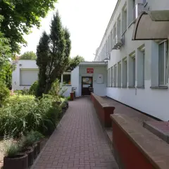 Wejście do Miejskiego Ośrodka Pomocy Rodzinie w Kielcach. Zadbany teren zielony i podjazd dla wózków.