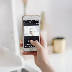 Dłoń trzyma smartfon, na ekranie którego widać interfejs aparatu. To może być pierwszy krok, by dowiedzieć się, jak przenieść zdjęcia z aparatu cyfrowego na telefon.
