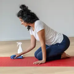 Frau reinigt ihre naturkautschuk yogamatte mit einem Tuch und Sprühflasche.