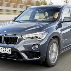 Szary BMW X1 z kierowcą za kierownicą jedzie po drodze. Zastanawiasz się, ile kosztuje BMW X1?