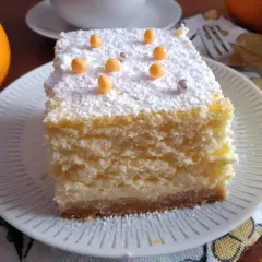 Pyszny sernik pieczony z delikatnym spodem z herbatników, posypany cukrem pudrem i pomarańczowymi kuleczkami.